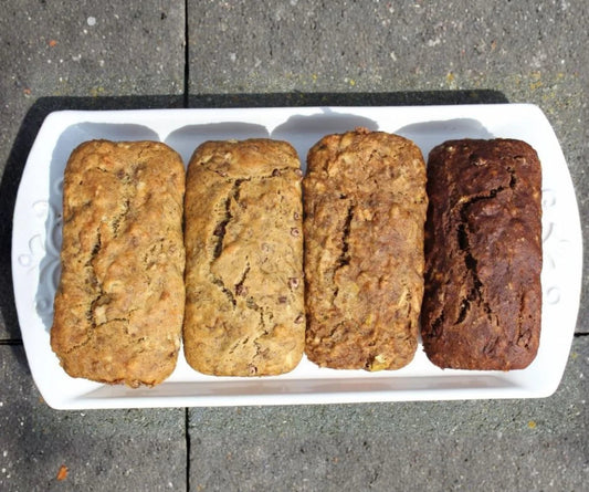 Four mini loaves of banana bread on a white plate outside.