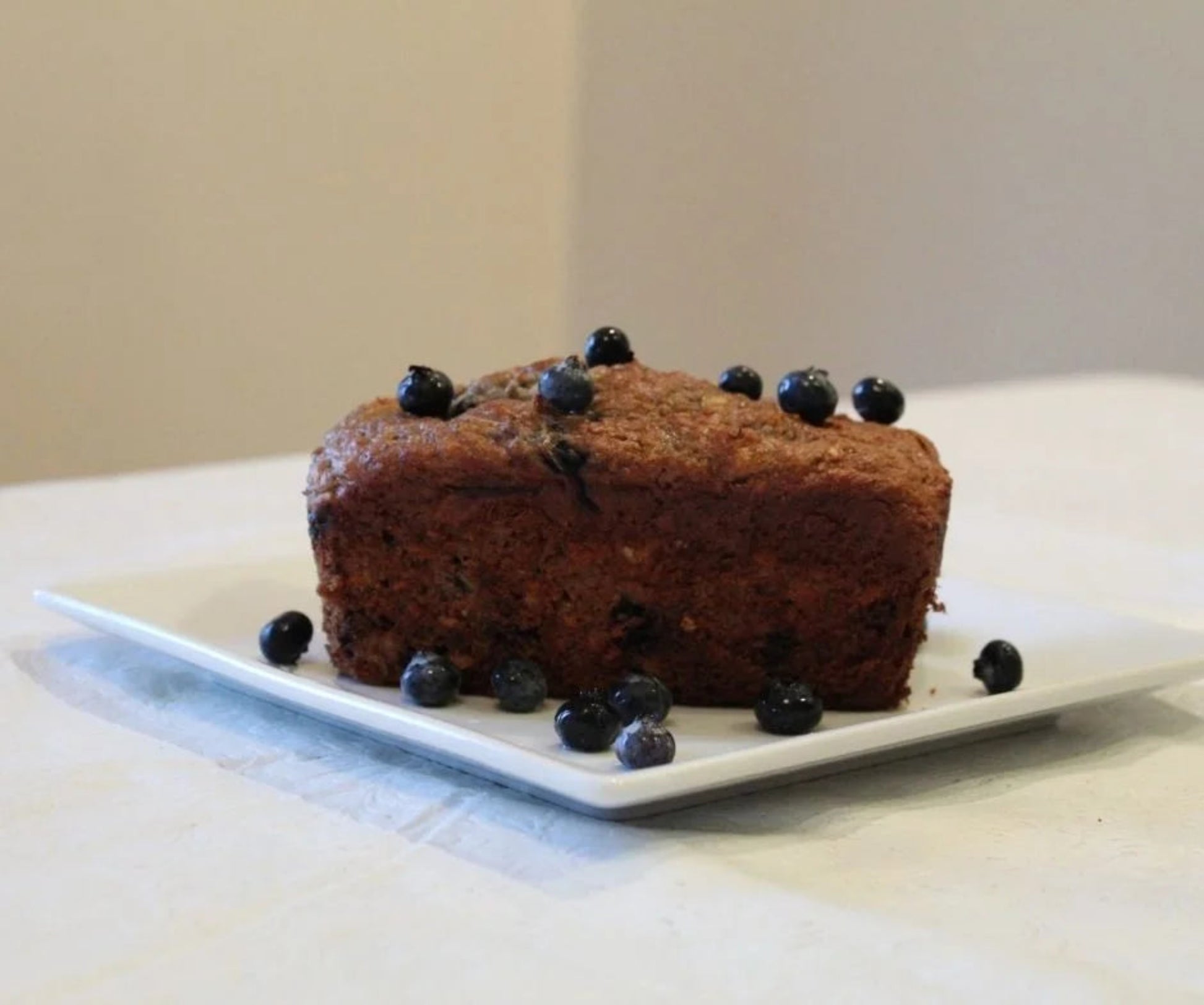 Min Loaf of bread with blueberries on a white plate.