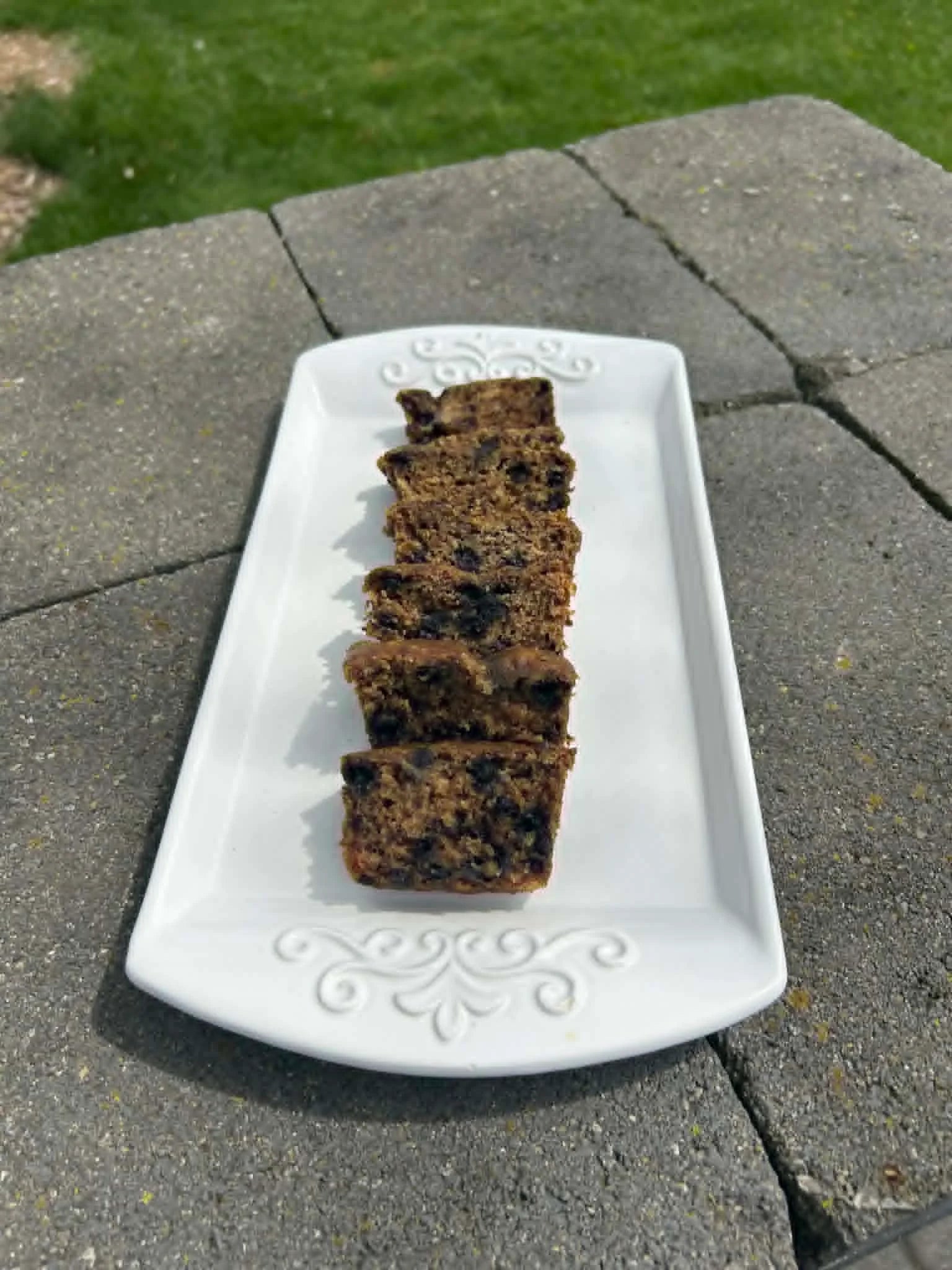Sliced blueberry banana bread on a decorative white plate outdoors.