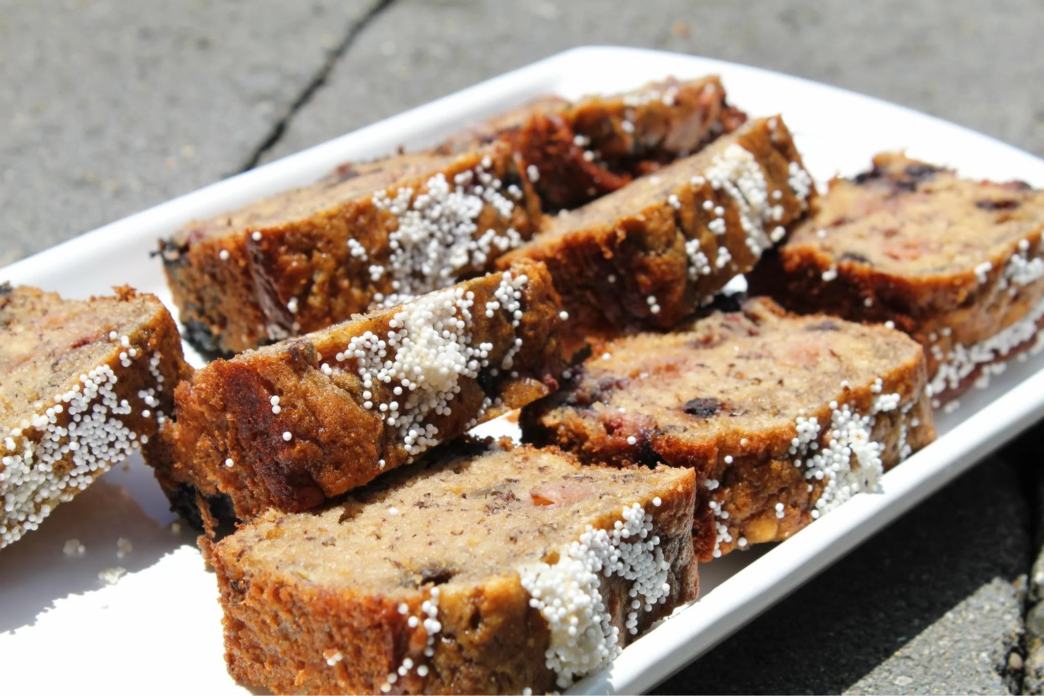 Slices of banana bread with sprinkles on a white tray outdoors.