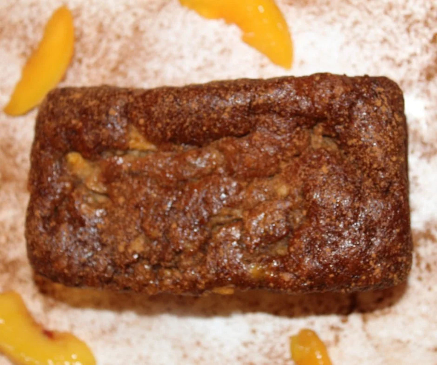 Loaf of Peach Cinnamon Banana Bread topped with dried peach slices and a sprinkle of cinnamon, served on a white plate.