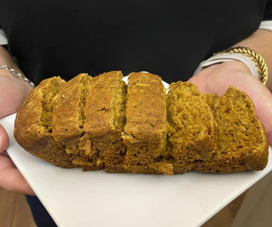 A loaf of pumpkin spice bread sliced on a white plate, held by a person wearing a black top.