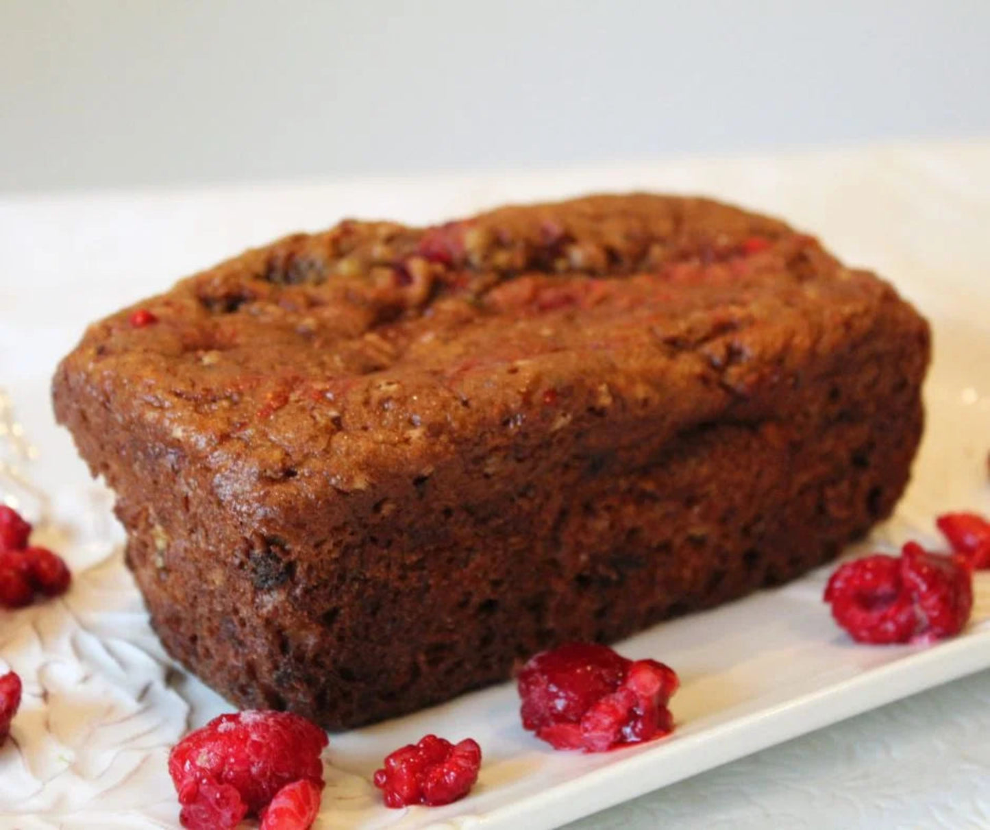 Loaf of raspberry banana bread on a white plate with raspberries.