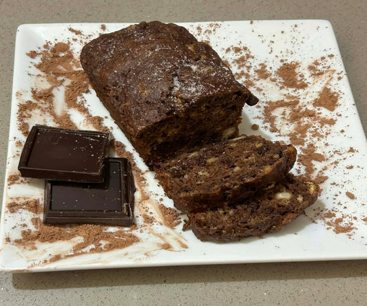 Loaf of chocolate cake with slices on a white marble slab, surrounded by chocolate pieces.