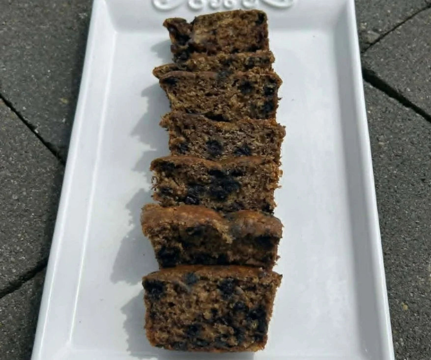Sliced mini blueberry banana bread on a decorative white plate outdoors.