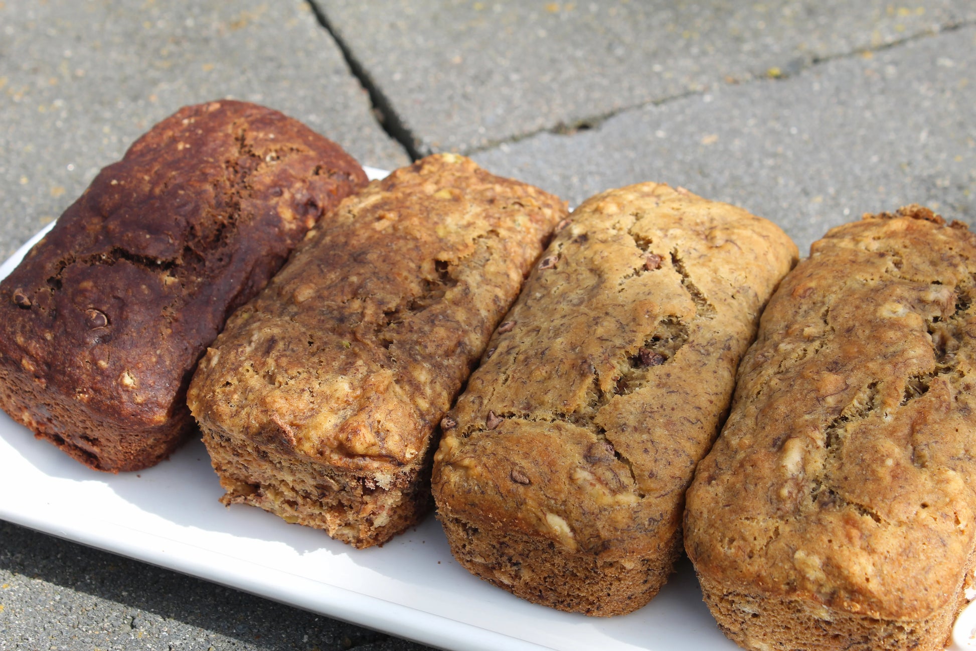 Four small loaves of bread on a white plate with a concrete floor background