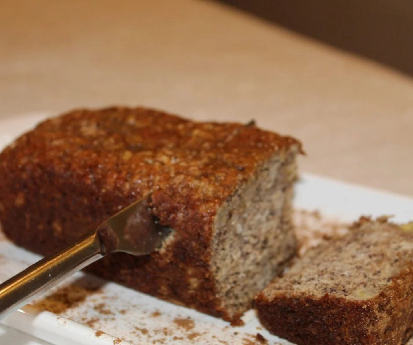 Loaf of banana bread with a slice cut, on a white plate with a fork.